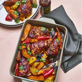 Juicy roasted chicken with colorful roasted vegetables in a ceramic baking dish, garnished with fresh herbs.