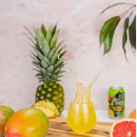 Fresh pineapple, mango, and grapefruit juice splash in a glass on a wooden board. Tropical fruits and a drink suggest refreshing, natural beverages from Cedar Works.