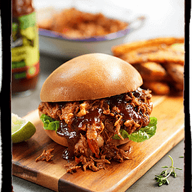 Tender slow-cooked beef burger with rich gravy, fresh greens, and toasted bun served on a wooden board, with sides of crispy fries and a dipping sauce, showcasing hearty comfort food from Cedar Works.