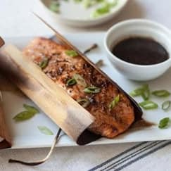 Smoked salmon fillet on cedar plank with fresh herbs, served with dipping sauce, highlighting Cedar Works' expertise in premium seafood and wood-fired cooking techniques.
