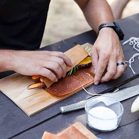 Sweet potato and vegetable wrap being assembled on cedar wood cutting board, showcasing outdoor cooking and food prep with natural timber surfaces.