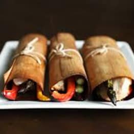 Freshly prepared sushi rolls wrapped in natural cedar bark, featuring vibrant vegetables and fresh seafood on a white plate.