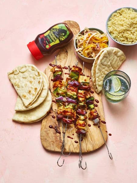 Grilled vegetable skewers with fresh pita bread, couscous, and a refreshing lemon water on a wooden serving board, featuring Cedar Works condiments and utensils.
