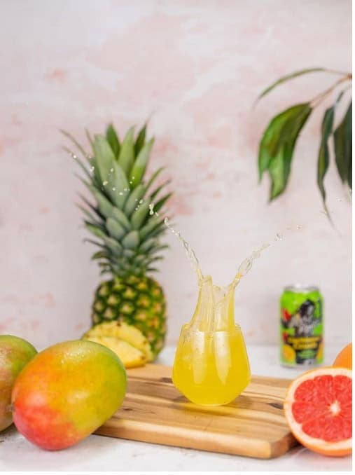 Fresh pineapple, mango, and grapefruit juice splash in a glass on a wooden board. Tropical fruits and a drink suggest refreshing, natural beverages from Cedar Works.