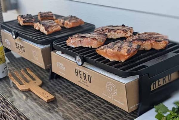 BBQ grills with grilled steaks and ribs on a wooden outdoor dining table, showcasing premium outdoor cooking and wood-fired grilling expertise by Cedar Works.